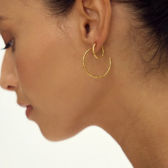 Close-up of a woman wearing gold hoop earrings on a neutral background
