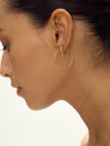 Close-up of a woman wearing gold hoop earrings on a neutral background