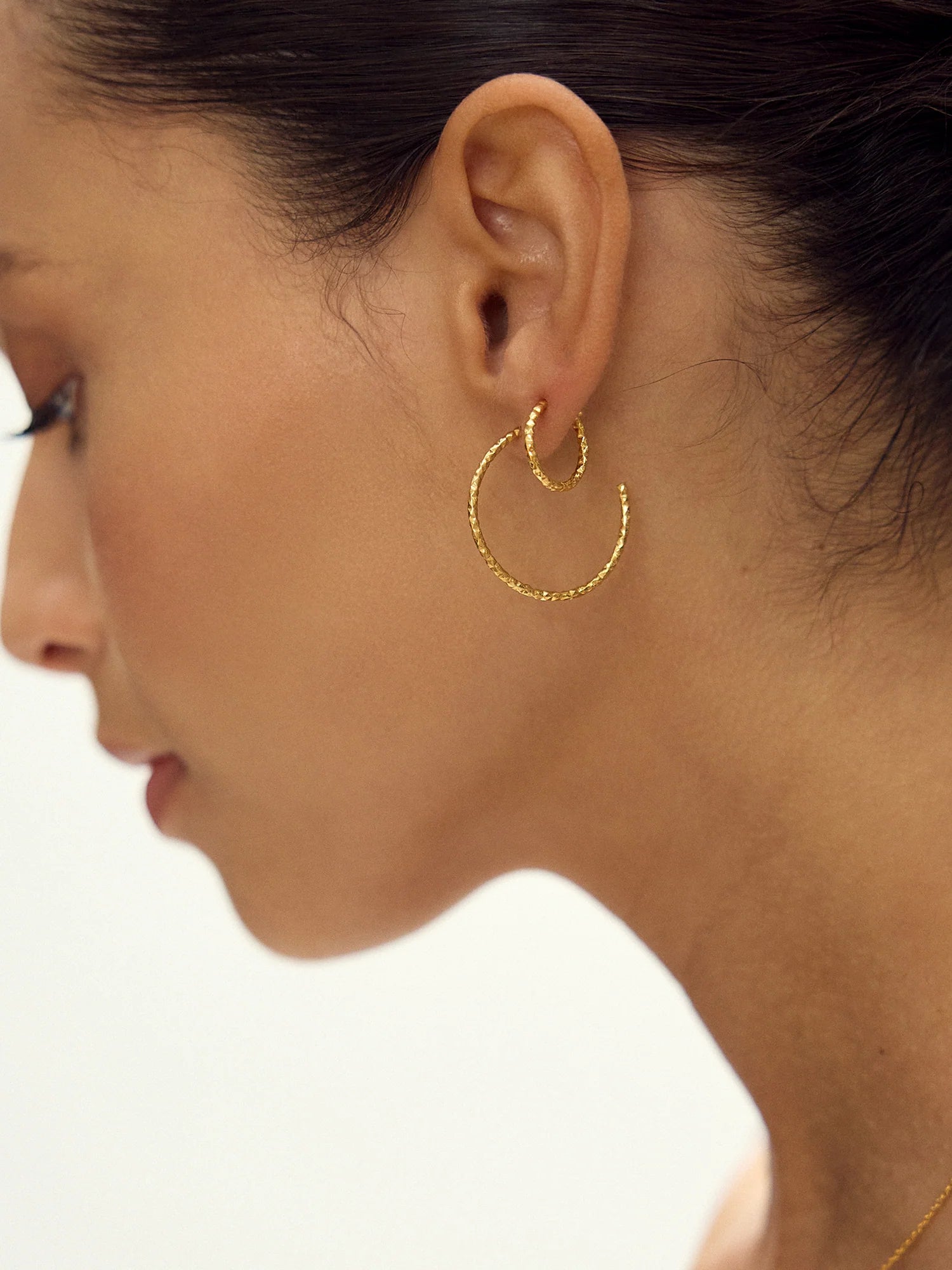 Close-up of a woman wearing gold hoop earrings on a neutral background