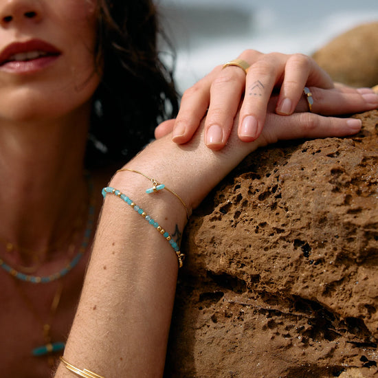 Woman with bracelets leaning against a rock by the water