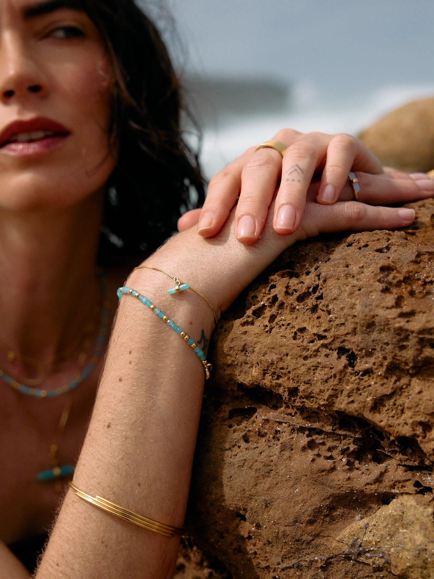 Woman with bracelets leaning against a rock by the water