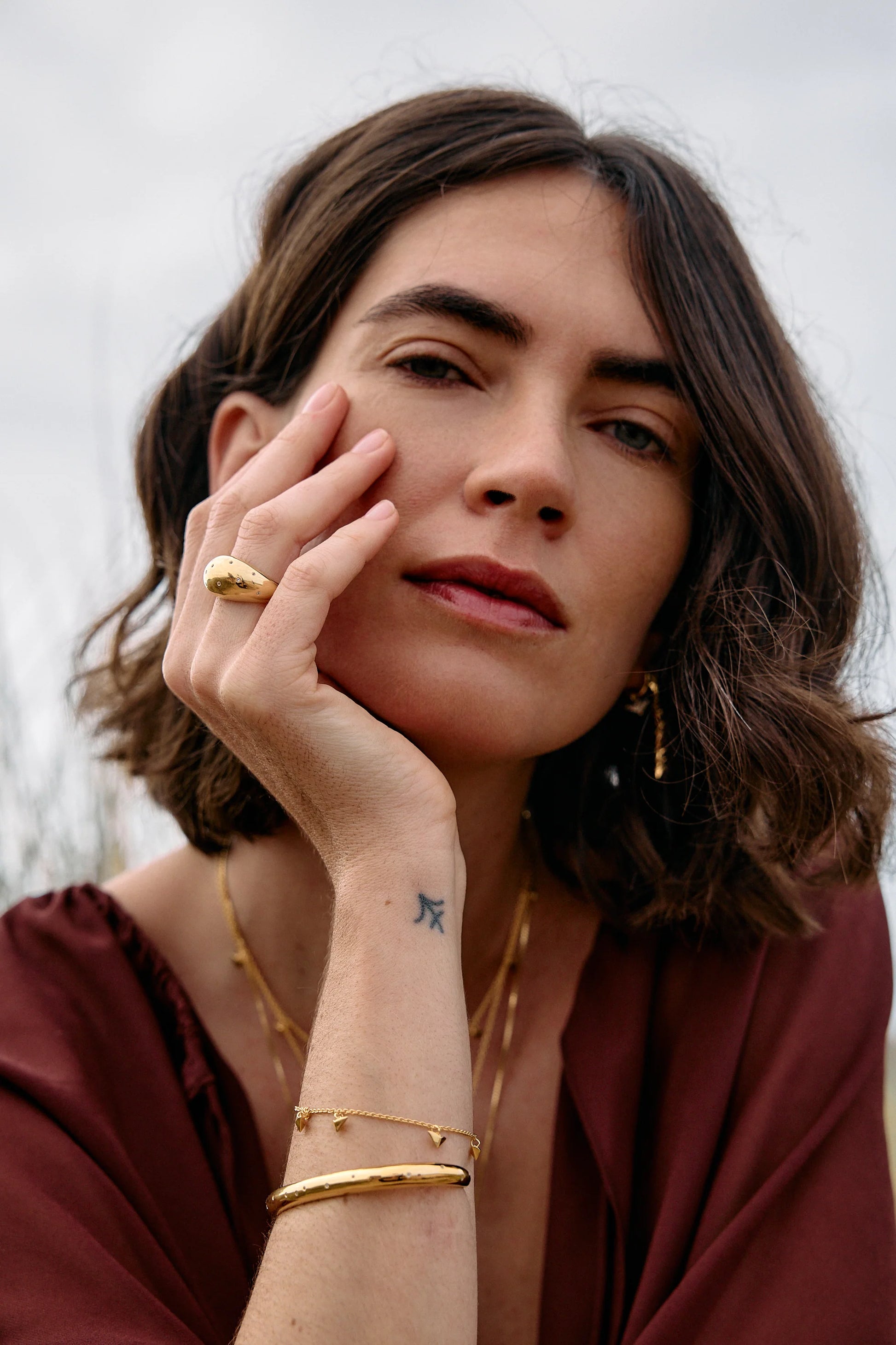 Rachel Jackson gold bird bracelet worn by a woman with other jewellery 