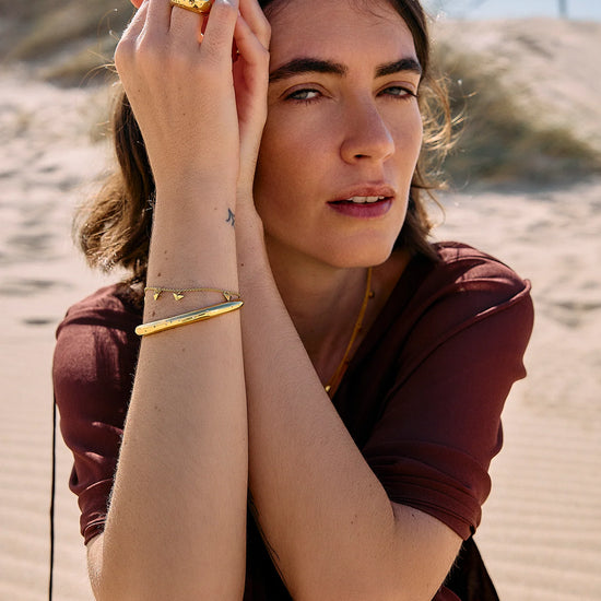 Rachel Jackson gold bird bracelet worn by a woman on the beach