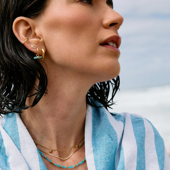 Woman wearing gold earrings and necklaces with a blue and white striped garment against a sky background