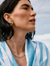 Woman wearing gold earrings and necklaces with a blue and white striped garment against a sky background