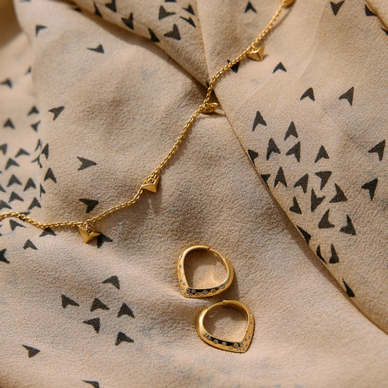 Gold necklace and earrings on a beige fabric with black triangle pattern