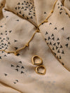 Gold necklace and earrings on a beige fabric with black triangle pattern