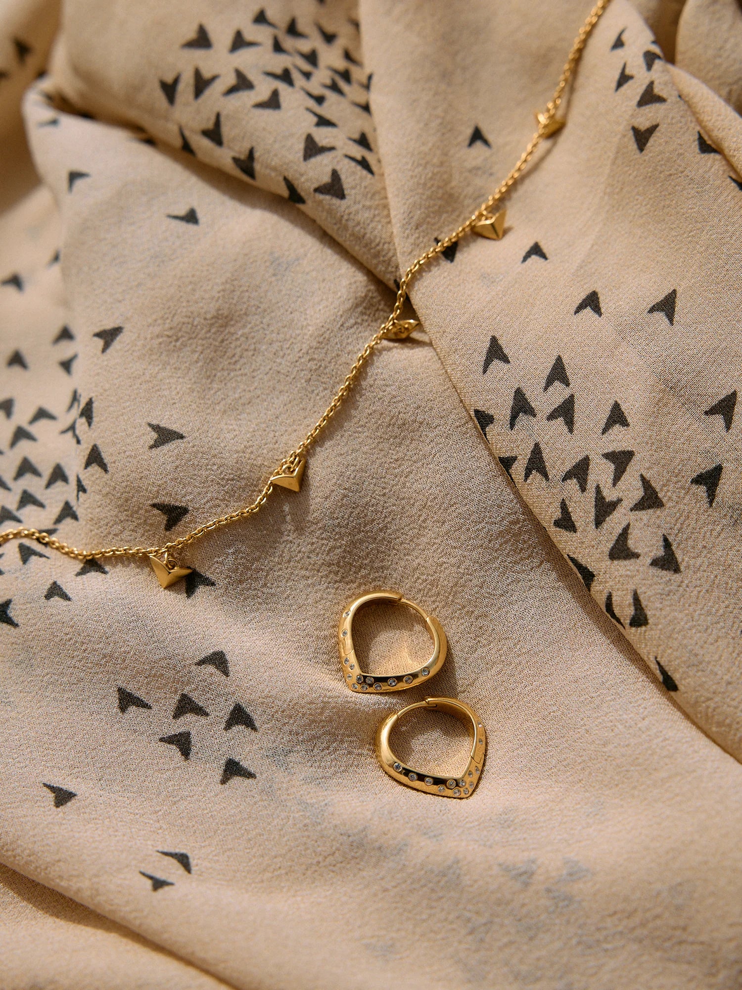 Gold necklace and earrings on a beige fabric with black triangle pattern
