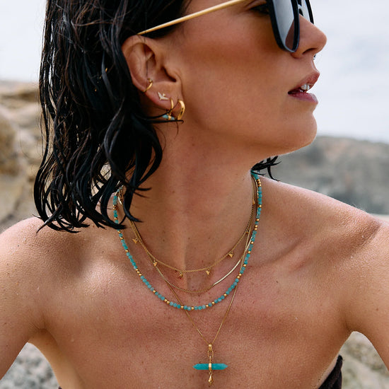 Woman wearing sunglasses and layered necklaces with a blurred natural background