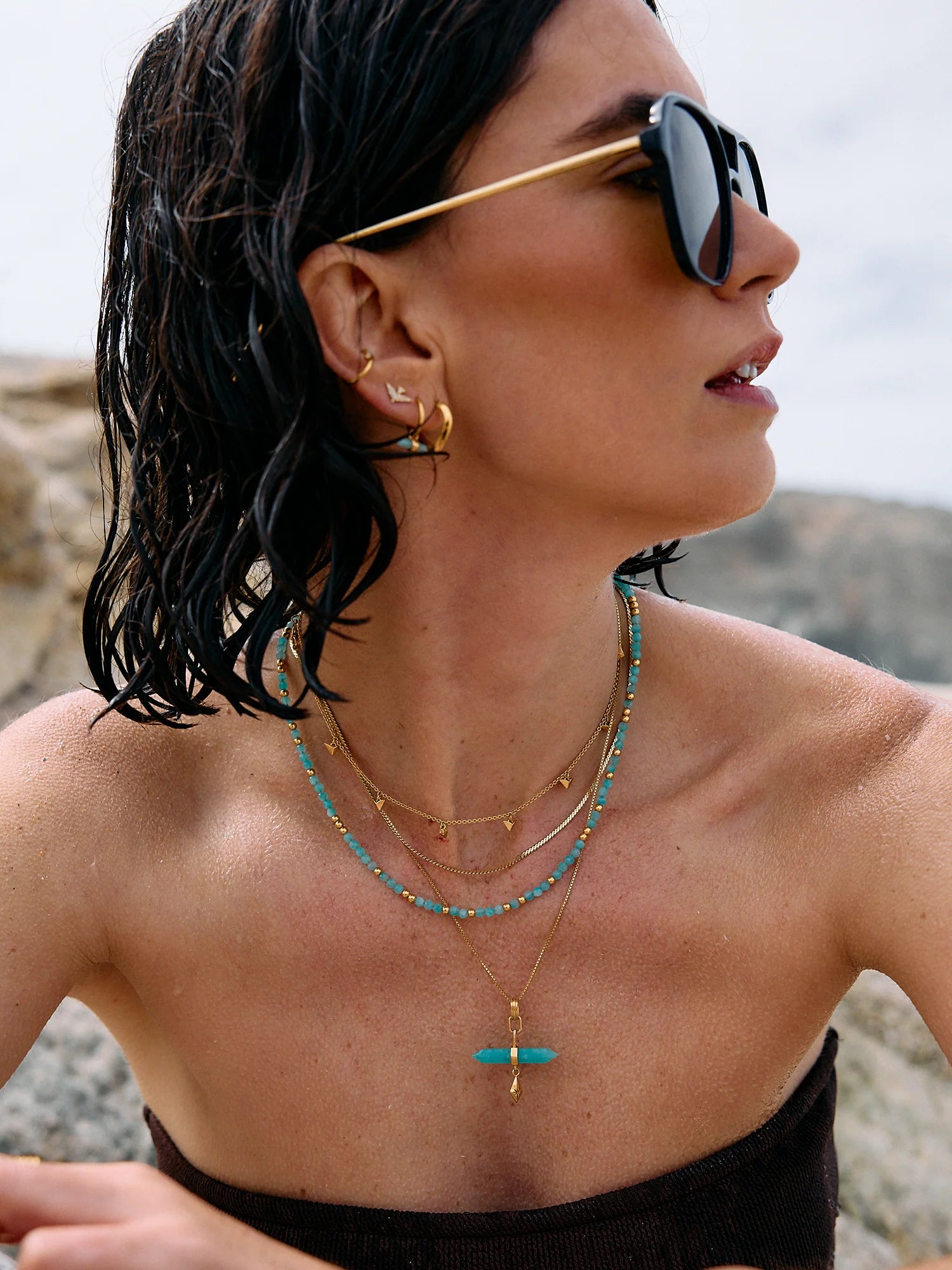 Woman wearing sunglasses and layered necklaces with a blurred natural background