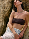 Woman wearing a brown bandeau top and white lace pants against a rocky background