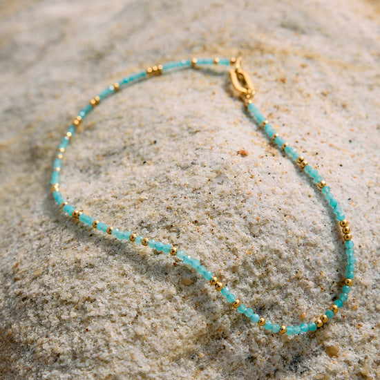 Turquoise beaded necklace with gold accents on a textured stone surface