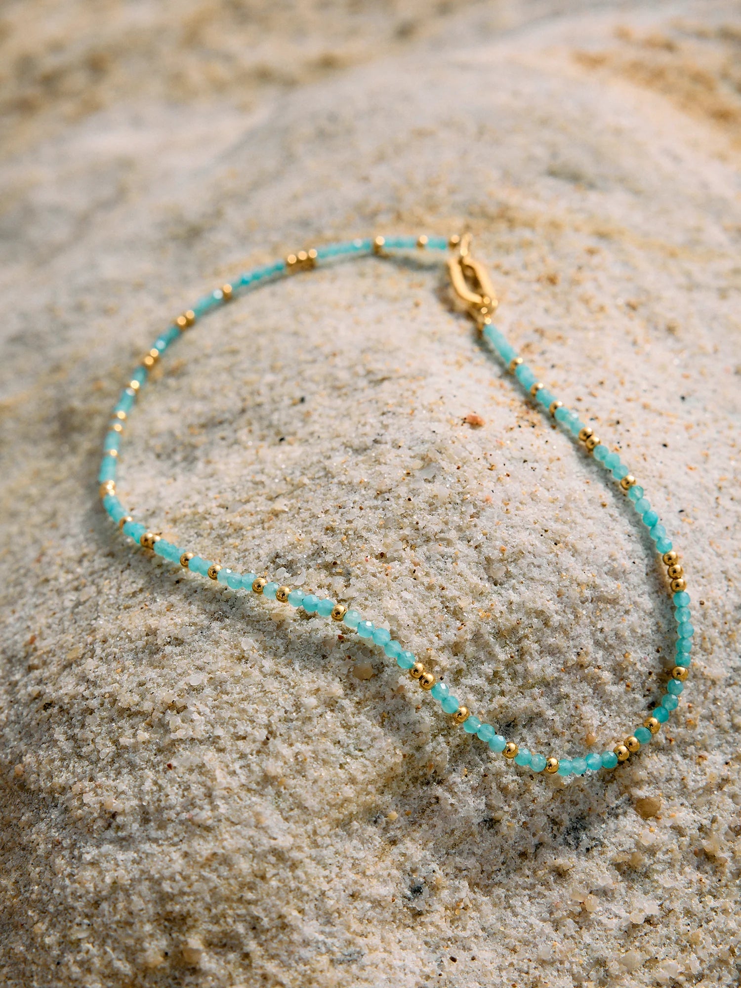 Turquoise beaded necklace with gold accents on a textured stone surface