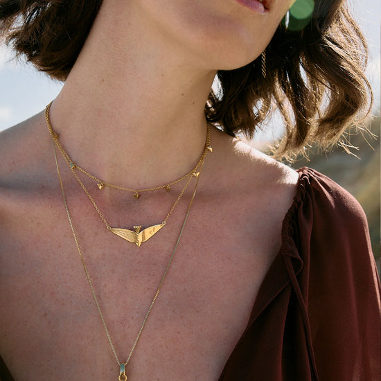 Close-up of a person wearing gold necklaces with a blurred natural background