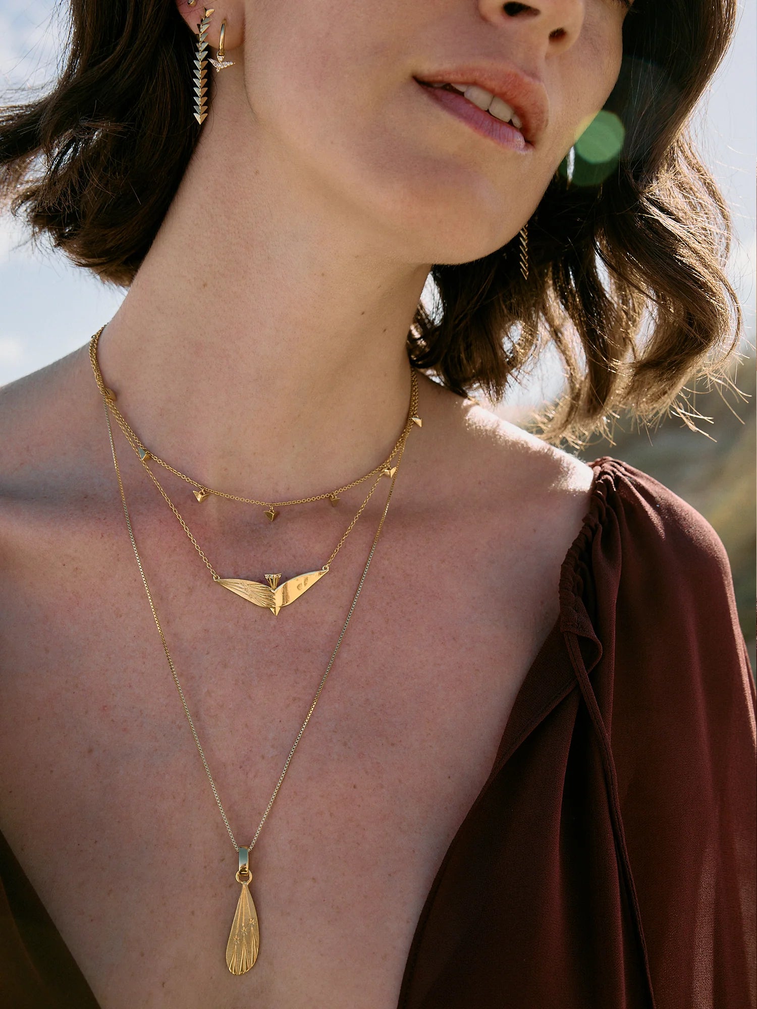 Close-up of a person wearing gold necklaces with a blurred natural background