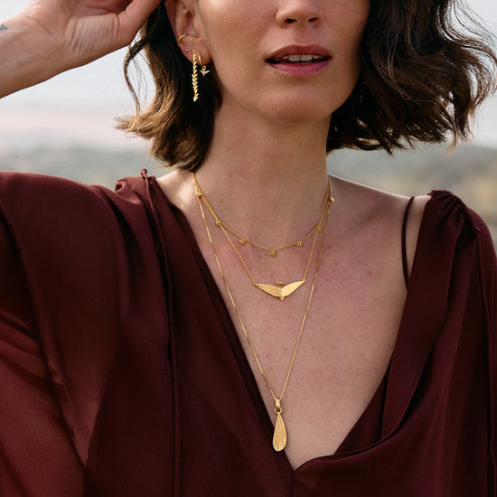 Woman wearing gold necklaces and earrings with a blurred natural background