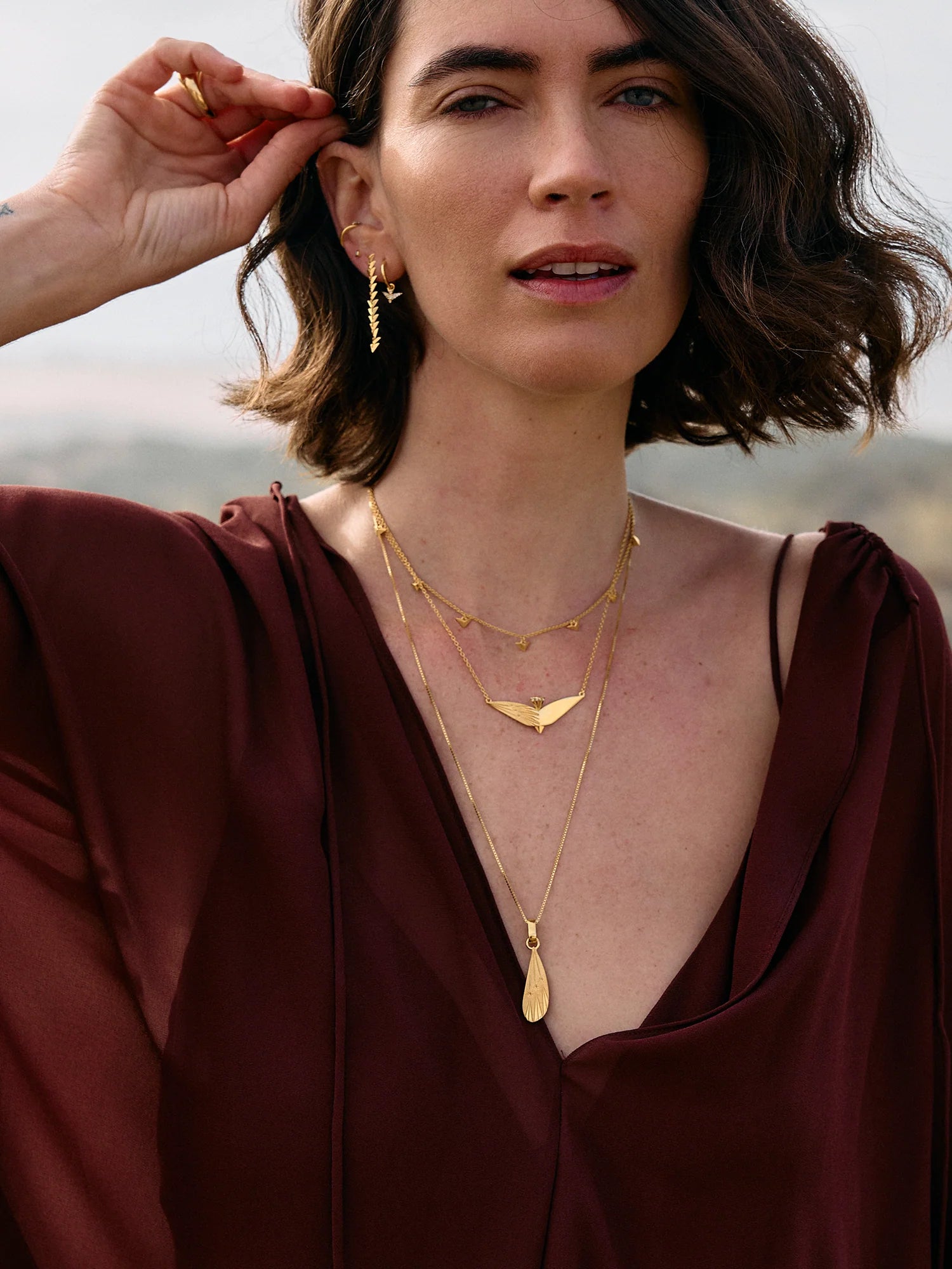 Woman wearing gold necklaces and earrings with a blurred natural background