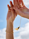 Gold necklace with a leaf pendant held by hands against a blue sky.