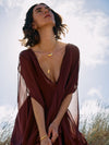 Woman wearing a burgundy dress with sheer sleeves against a blurred natural background