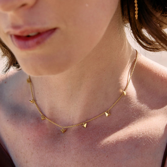 Close-up of a person wearing a gold necklace with small triangle pendants.