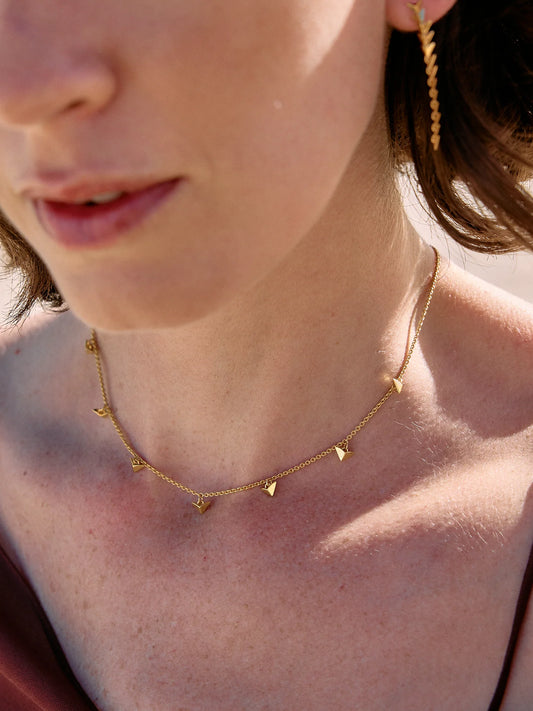 Close-up of a person wearing a gold necklace with small triangle pendants.