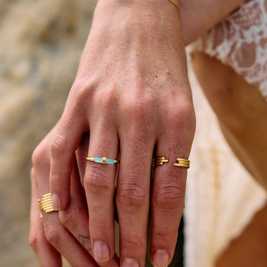 Close-up of a hand wearing gold rings with a blurred natural background