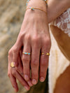 Close-up of a hand wearing gold rings with a blurred natural background