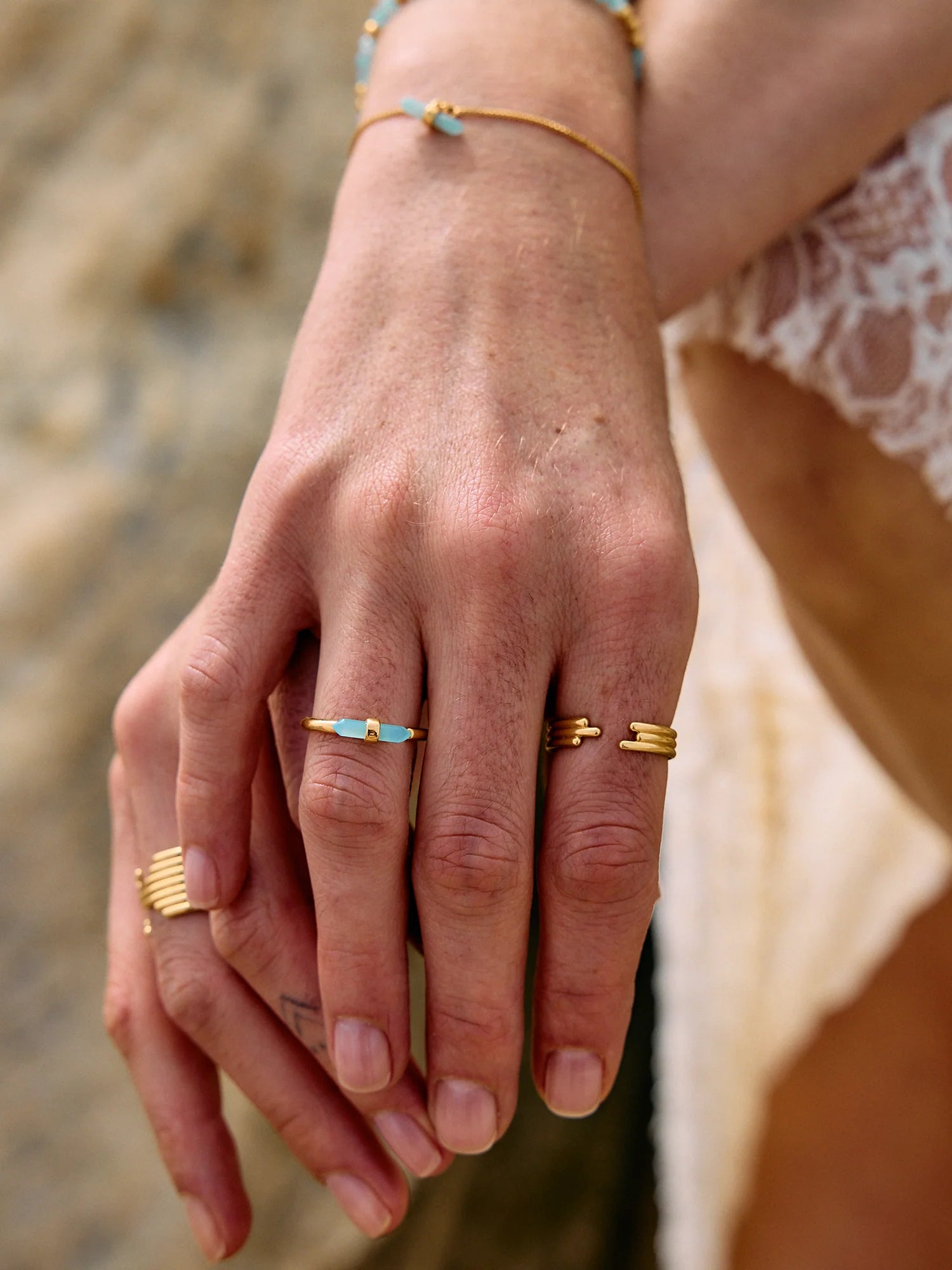Close-up of a hand wearing gold rings with a blurred natural background