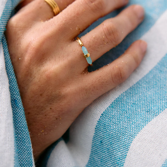 Hand wearing a gold ring with a blue stone on a blue and white striped fabric background