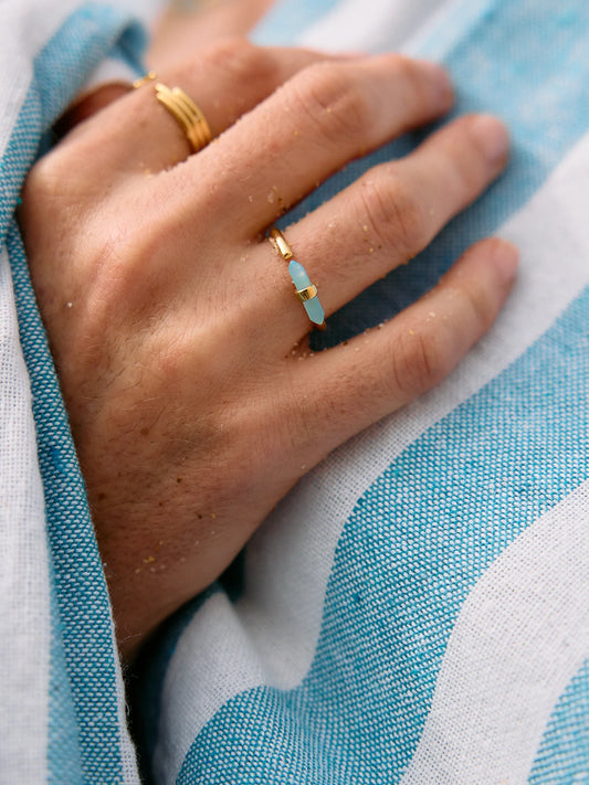 Hand wearing a gold ring with a blue stone on a blue and white striped fabric background