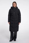 A woman modeling a long black hooded puffer coat with a front zipper, paired with black pants, against a plain light gray studio background.