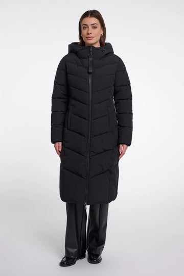 A woman modeling a long black hooded puffer coat with a front zipper, paired with black pants, against a plain light gray studio background.