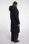 A model shown from the back wearing a long black puffer coat with a hood, paired with dark wide-leg trousers, against a plain light gray studio background.