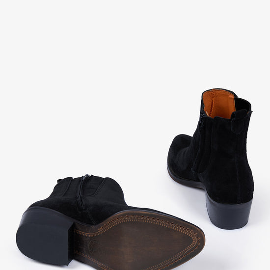 A pair of black suede ankle boots shown from the side and back on a clean white background, displaying the black sole and a contrasting orange-brown interior lining.