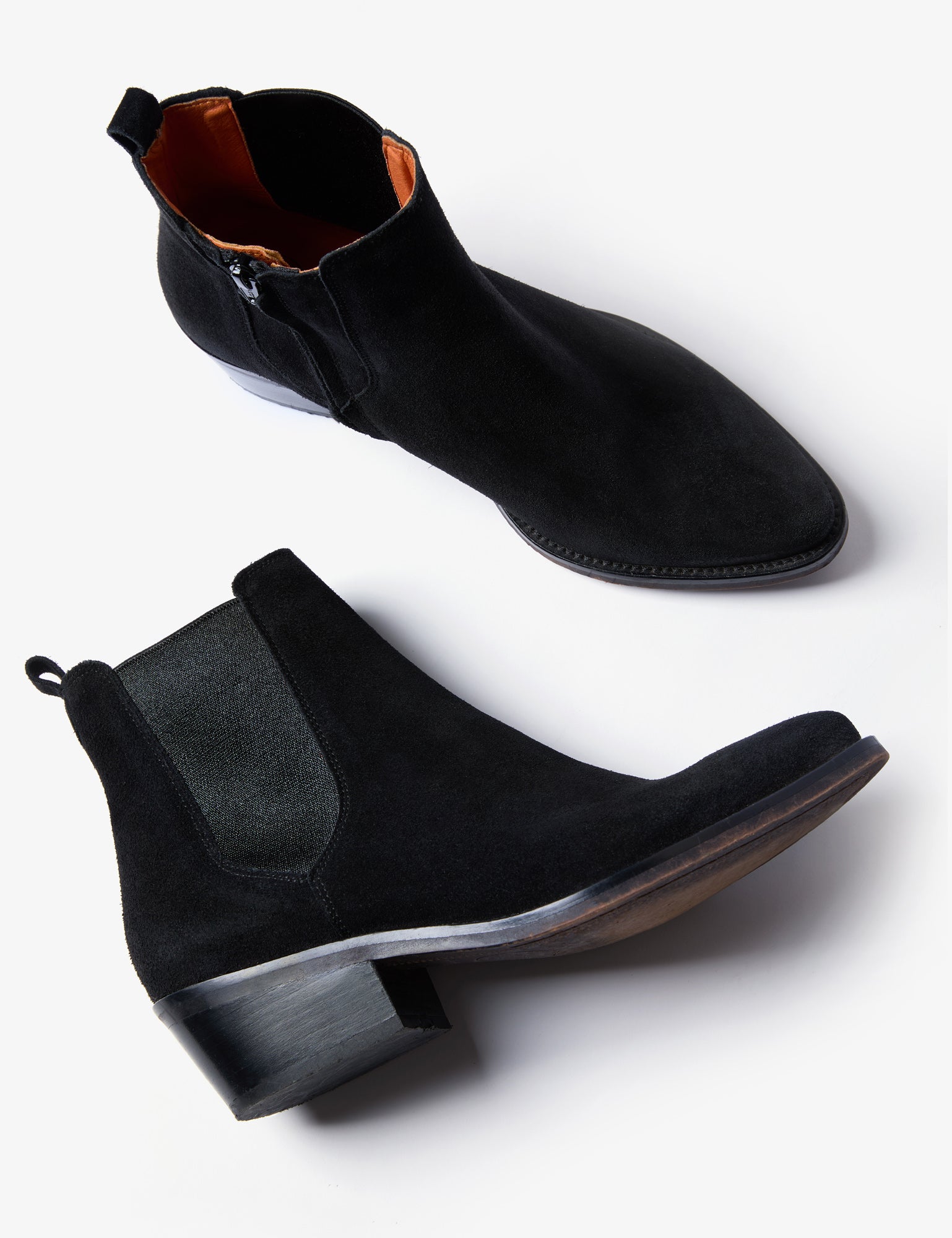 A pair of black suede Chelsea-style ankle boots with elastic side panels and low block heels, shown from side and angled top views on a light gray background.