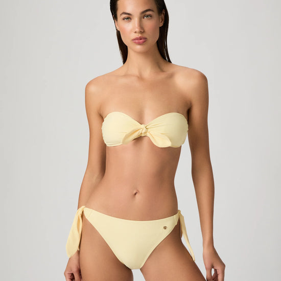 Woman wearing a yellow bikini from Paige against a gray background
