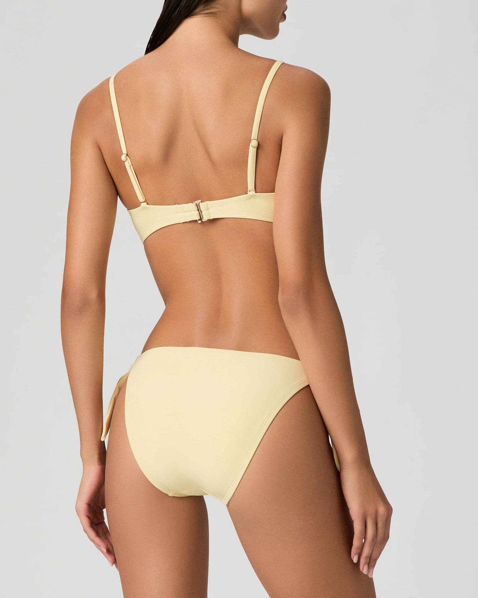 Woman wearing a yellow bikini from Paige against a plain background