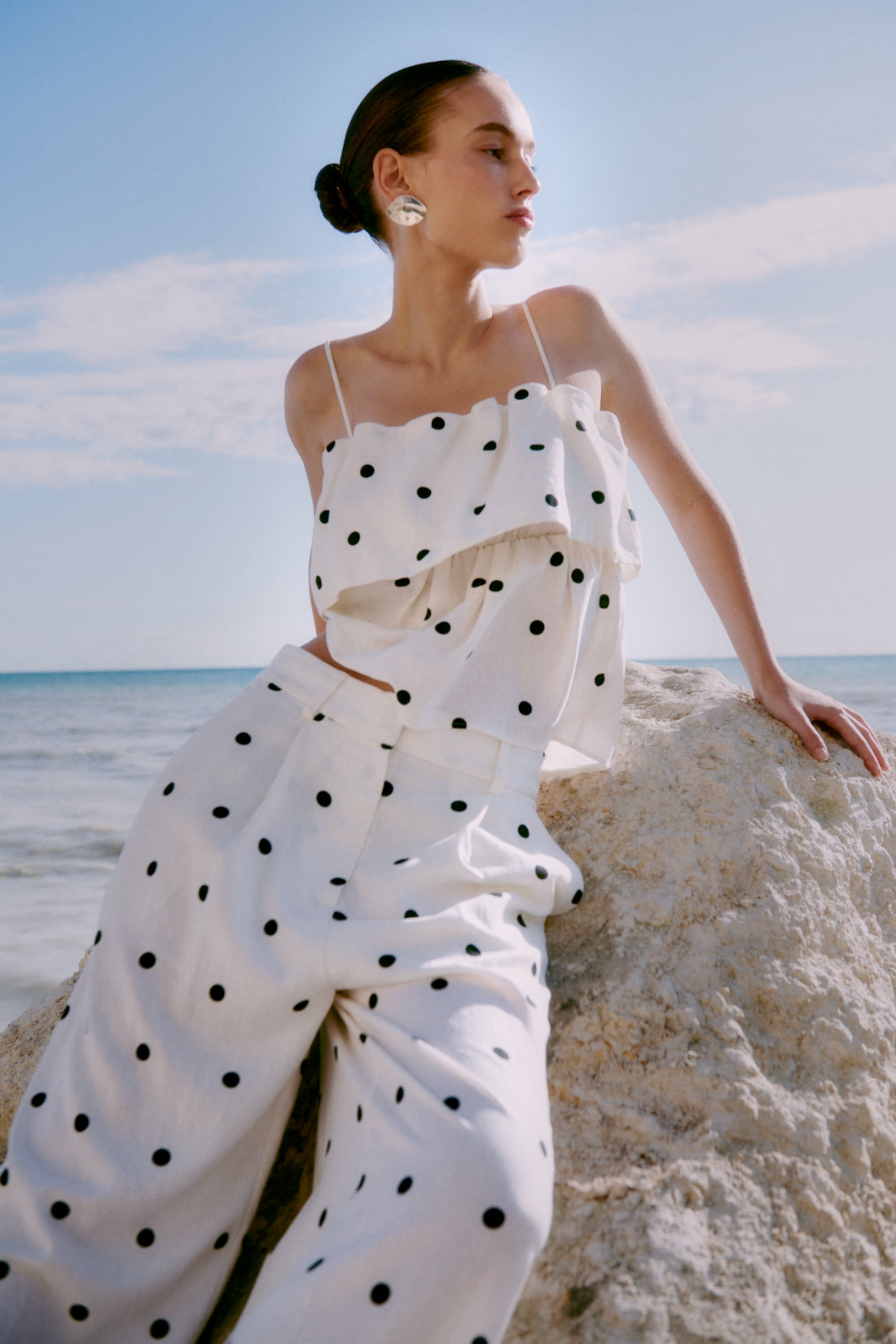 Woman in a polka dot co-ord standing on a sandy beach with ocean view