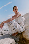 Woman in a polka dot co-ord
 sitting on rocks by the beach