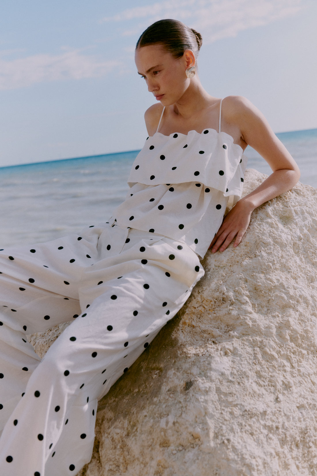 Woman in a polka dot dress sitting on sand with ocean in the background