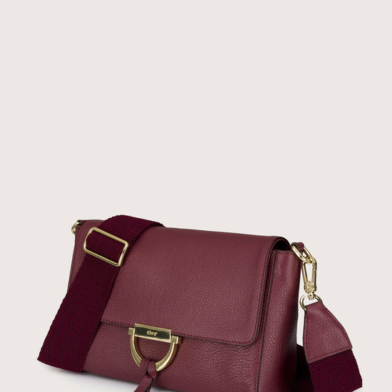 Burgundy handbag with gold accents on a light beige background