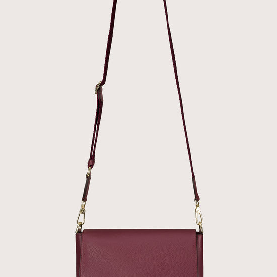 Maroon handbag with a strap on a light gray background