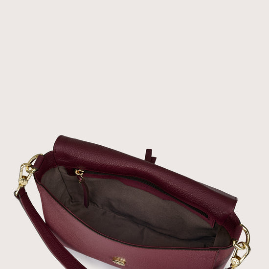 Maroon handbag with gold accents on a light beige background