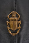black leather fold over bag with gold scarab stamp and linen strap close up of scarab