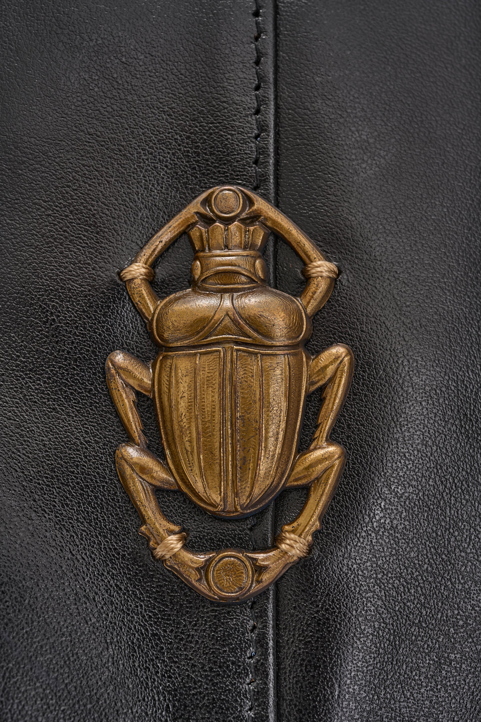 black leather fold over bag with gold scarab stamp and linen strap close up of scarab