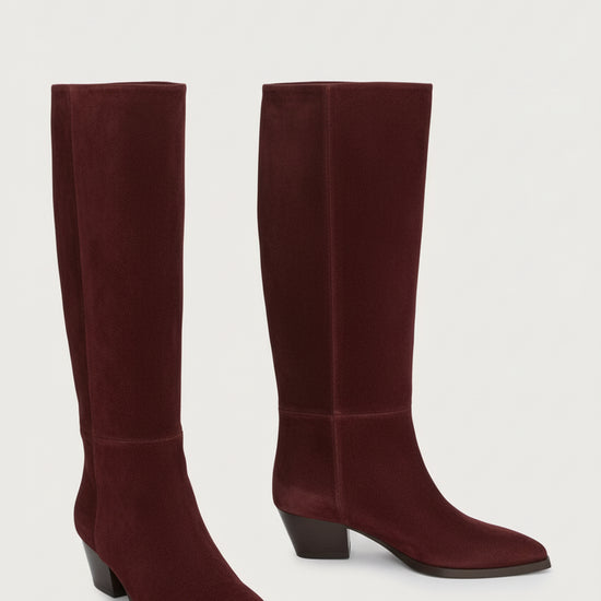 Pair of maroon suede knee-high boots on a light gray background