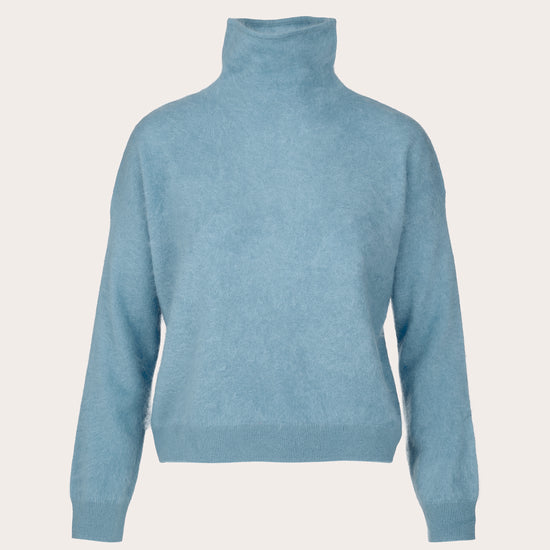 A light blue knit turtleneck sweater shown from the back on a clean, solid, warm off-white background.