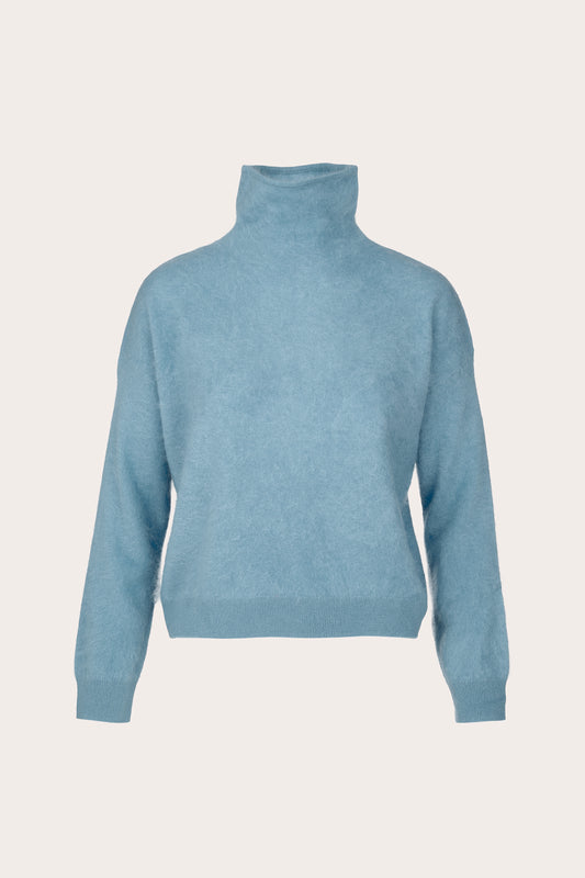 A light blue knit turtleneck sweater shown from the back on a clean, solid, warm off-white background.