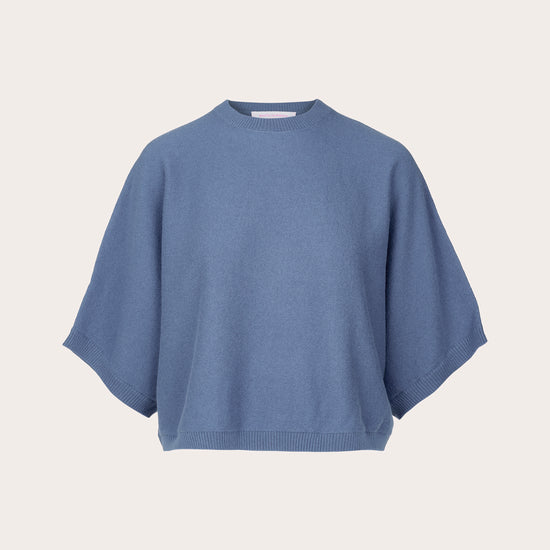 A dusty blue knit sweater with a relaxed, oversized fit and wide short sleeves, presented on a clean, solid off-white background.
