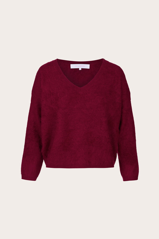 A textured knit V-neck sweater in deep burgundy, displayed flat against a light cream background.